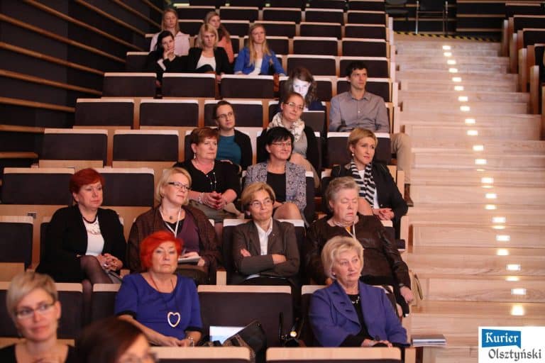 Grupa kobiet siedzi na sali konferencyjnej podczas wydarzenia w Filharmonii w Olsztynie.