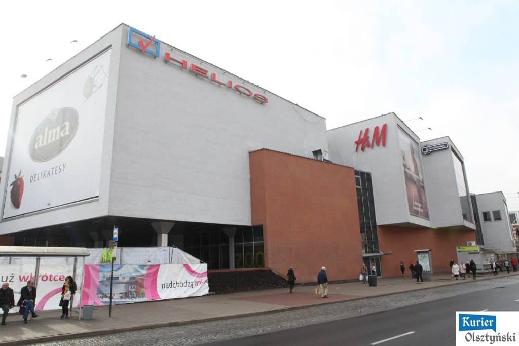 Widok na zewnątrz centrum handlowego Aura z ludźmi przechodzącymi chodnikiem.