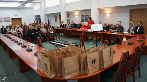 Uczestnicy konkursu krasomówczego siedzą na sali podczas prezentacji przed jury, obok stoją torby z pakietami.