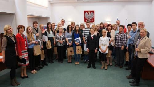Grupa uczniów i nauczycieli na konkursie krasomówczym w sali w Olsztynie.