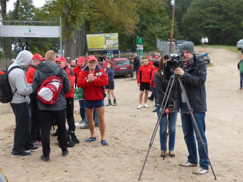 Grupa morsów i widzów podczas inauguracji sezonu zimowych kąpieli na plaży, z kamerzystą rejestrującym wydarzenie.