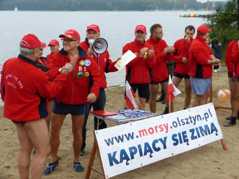 Morsy z Olsztyna w czerwonych kurtkach i czapkach na plaży podczas inauguracji sezonu zimowych kąpieli.