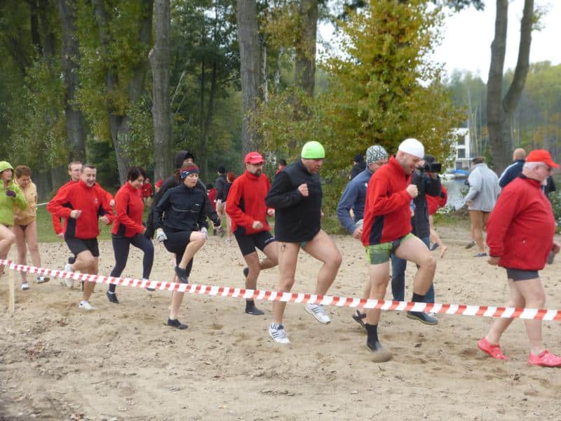 Grupa ludzi w ciepłych ubraniach i czapkach, biegających na plaży podczas inauguracji sezonu zimowych kąpieli.