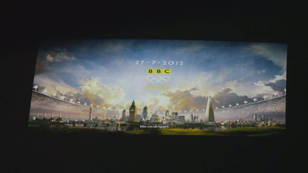 Slajd projekcji z festiwalu BlueBox 2013 w olsztyńskim Planetarium, przedstawiający londyńskie symbole i logo BBC, datę i wiadomość.