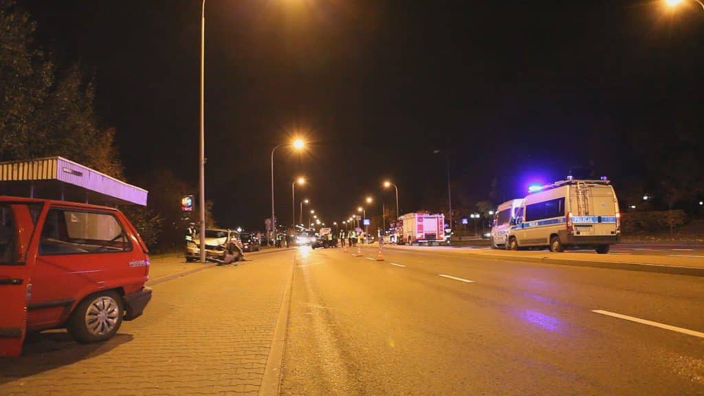 Widok na zablokowaną ulicę Sielską po kolizji, na miejscu pojazdy ratunkowe, straż pożarna i policja, wieczorem.