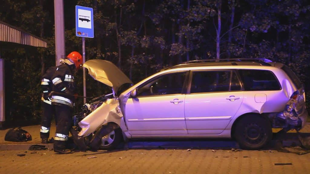 Samochód po kolizji na ulicy Sielskiej, uszkodzona przednia część pojazdu, strażak bada stan samochodu.