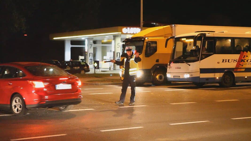 Tłum na ulicy Sielskiej po kolizji czterech samochodów, policjant kieruje ruchem w nocy.
