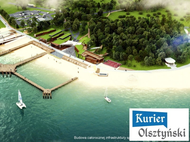Widok na plażę miejską z piaskiem, opiekanymi terenami zielonymi i łódkami na wodzie.