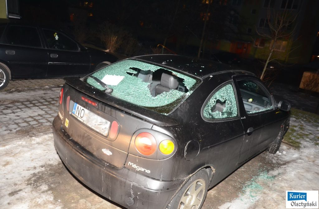 Uszkodzony czarny samochód z wybitymi szybami na parkingu nocą.