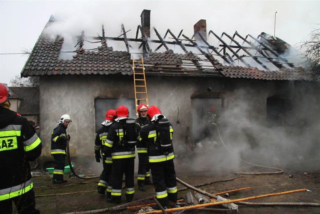 Strażacy gaszą pożar domu jednorodzinnego w Spręcowie, widoczny dym i zniszczony dach.