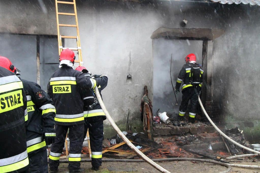 Strażacy gaszą pożar w domu w Spręcowie, widoczne zadymienie i zniszczenia po pożarze.