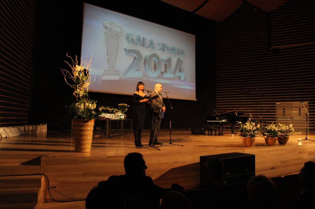 Na scenie w filharmonii dwie osoby mówią do publiczności, za nimi ekran z napisem 'Gala Sportu 2014'.