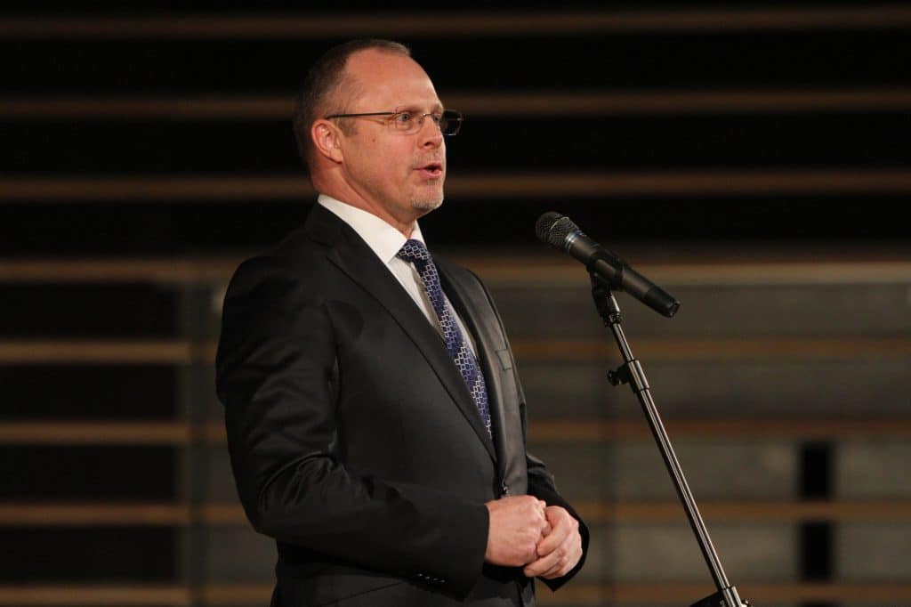 Mężczyzna w garniturze przemawia podczas gali sportu w filharmonii, stojąc przy mikrofonie.