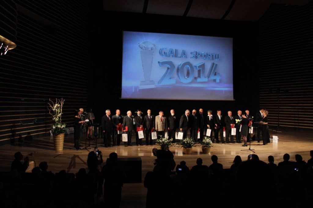 Grupa sportowców i urzędników na scenie podczas gali w filharmonii, z dużym ekranem wyświetlającym napis Gala Sportu 2014.