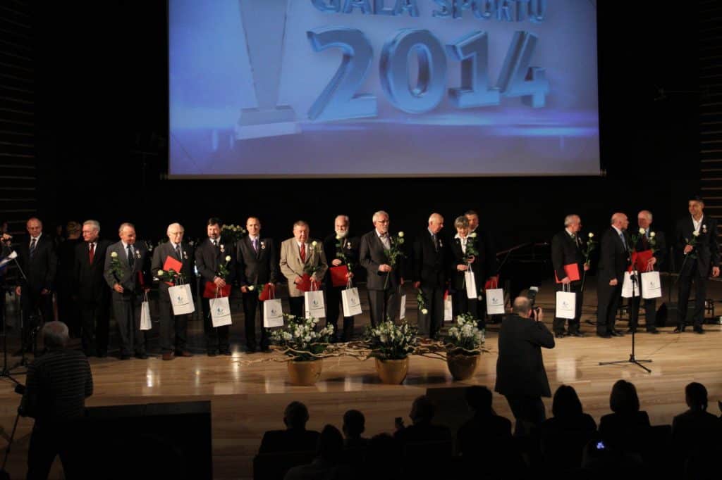 Grupa sportowców stojących na scenie podczas gali, trzymających kwiaty i odznaczenia.