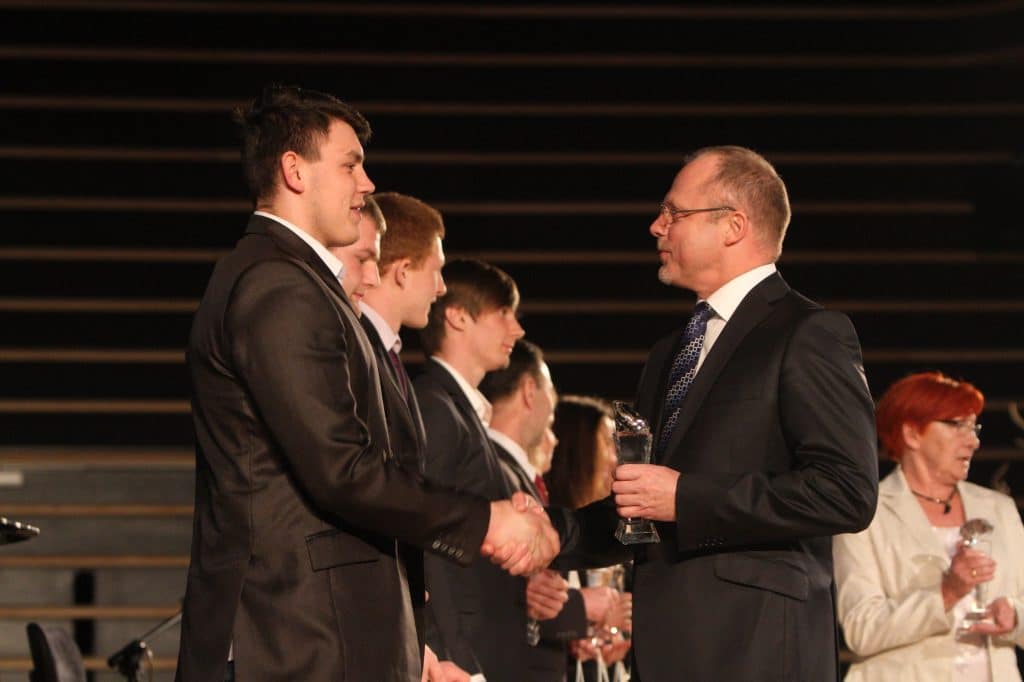 Mężczyzna wręcza odznakę młodemu sportowcowi podczas gali w filharmonii.