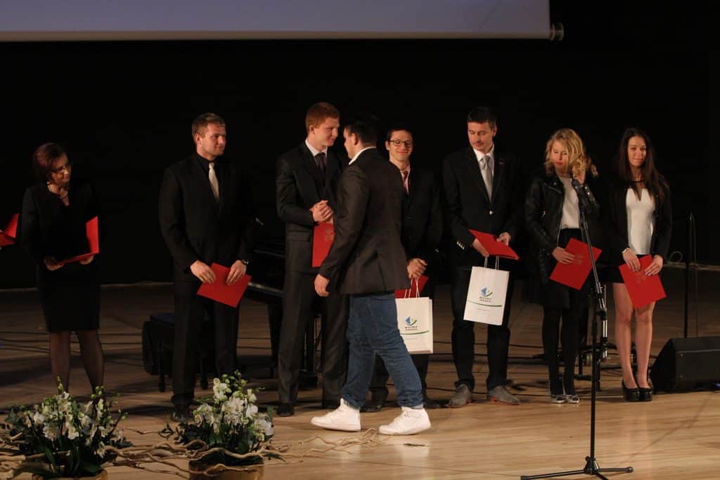 Uczestnicy gali sportu w czasie wręczania nagród na scenie w filharmonii, w tle czarna kurtyna.