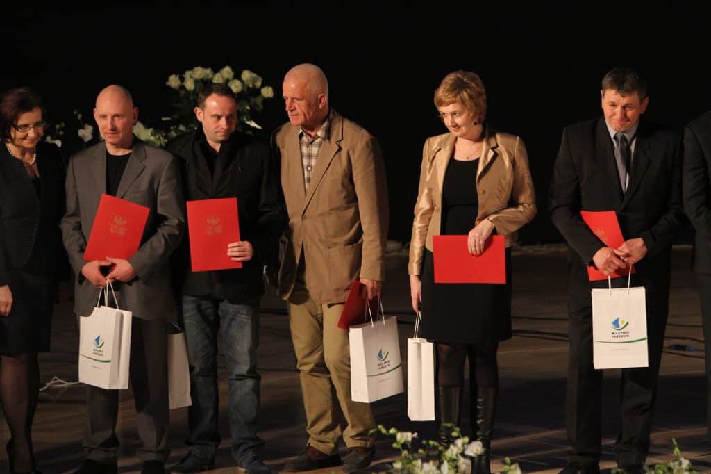 Zdjęcie grupowe wyróżnionych sportowców i gości na gali w filharmonii, trzymających nagrody i dyplomy.