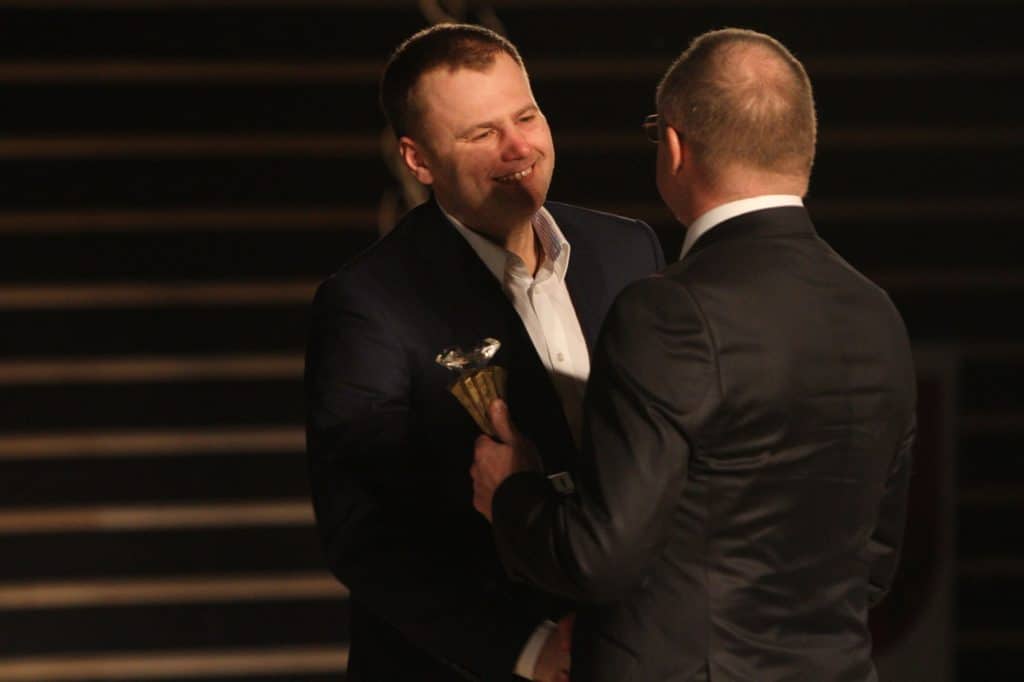 Mężczyzna z uśmiechem otrzymuje odznakę podczas Gali Sportu 2014 w filharmonii.