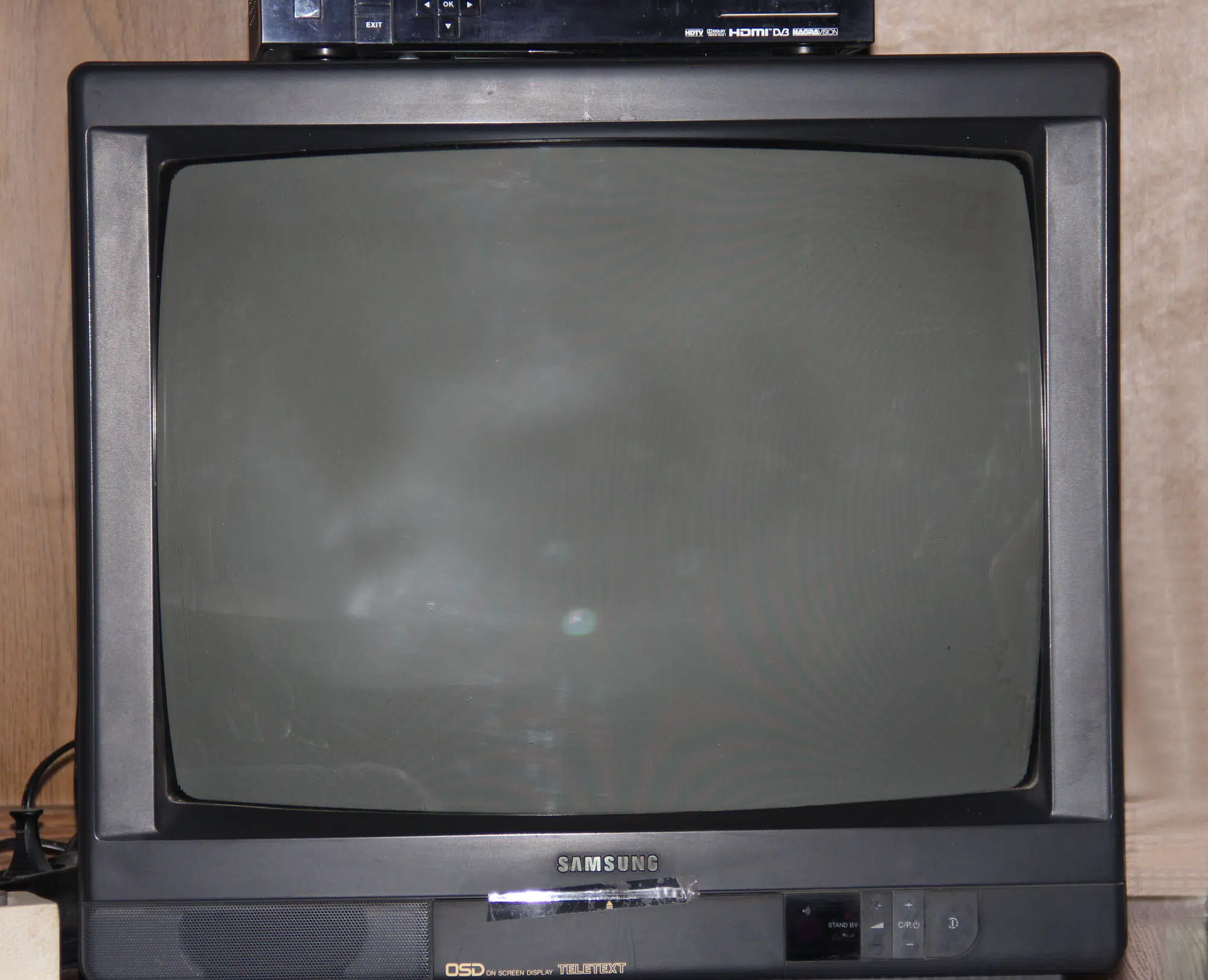 Stary telewizor marki Samsung na tle drewnianej ściany.