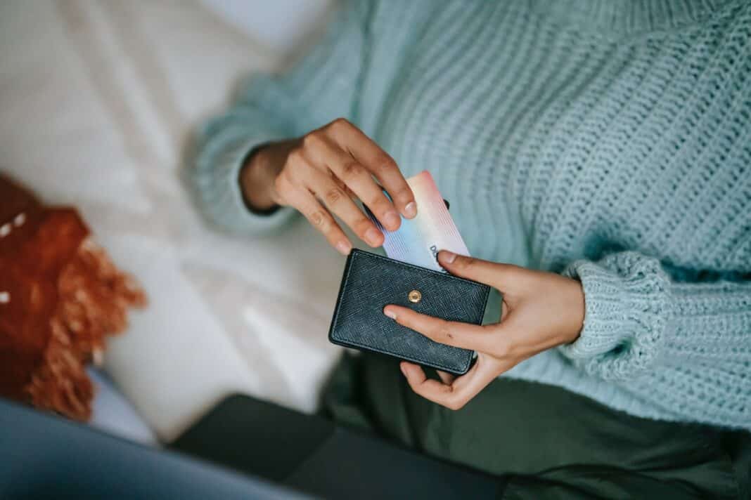 Młoda osoba wyciąga kartę z portfela na tle laptopa.