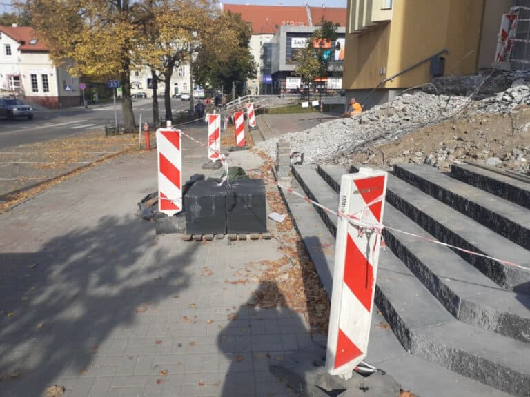 Remont schod&oacute;w do centrum handlowego Manhattan, część chodnika zablokowana barierkami i workami z materiałami budowlanymi.