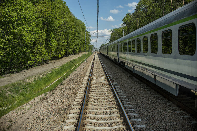 Pociąg na torach w otoczeniu zielonych drzew, widok z perspektywy na linie kolejowe.