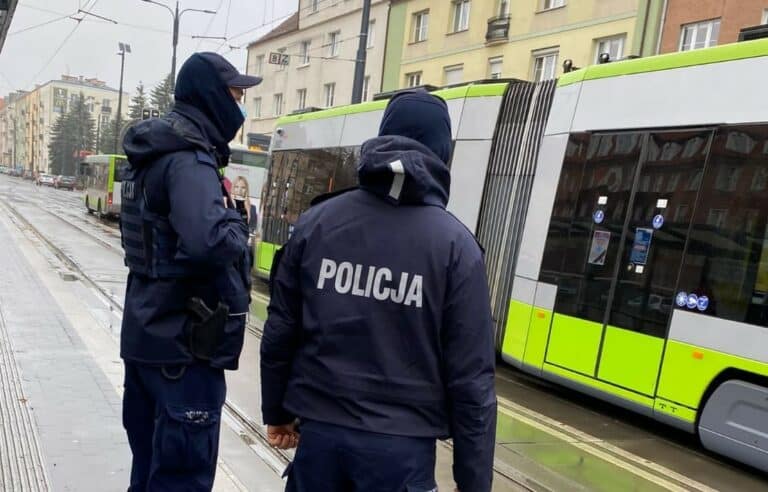 Policjanci kontrolują pasażer&oacute;w w miejskim autobusie w Olsztynie, na tle tramwaju i miejskiej ulicy.