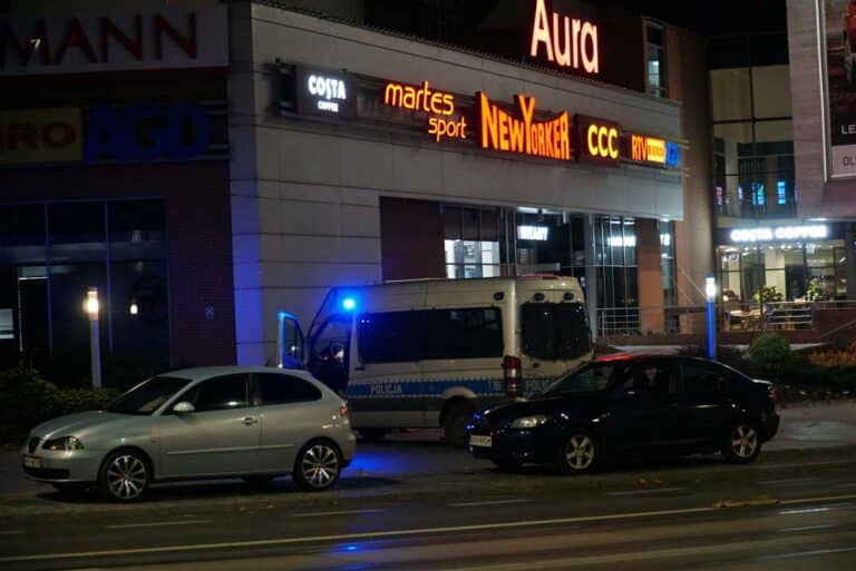 Mężczyzna obnaża się przed Centrum Handlowym Aura w Olsztynie, na miejscu policja i samochody służbowe.