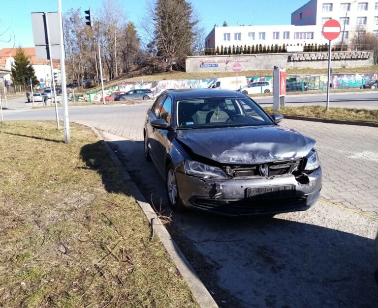 Uszkodzony samoch&oacute;d na poboczu przy stacji benzynowej, widoczne wgniecenia na maskę i zderzaku.