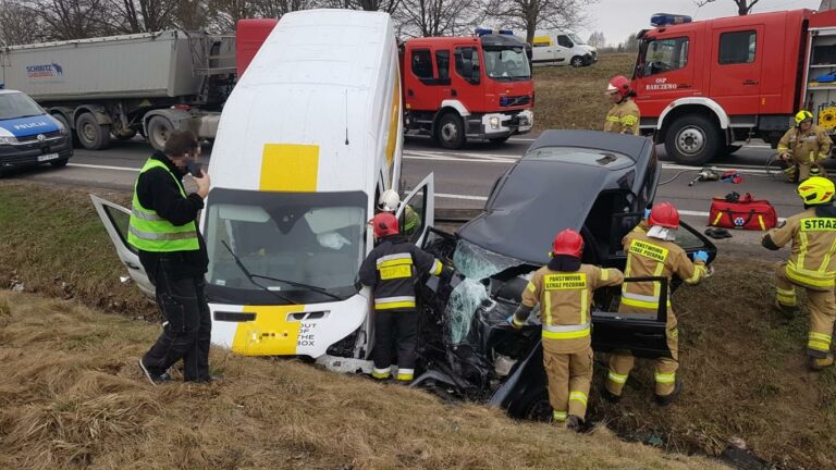 Zdjęcie z miejsca wypadku na DK 16, z rozbitymi pojazdami i służbami ratunkowymi na miejscu.