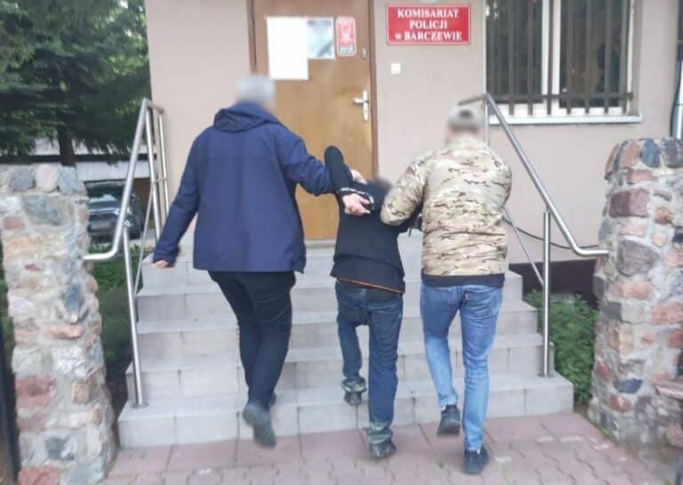 Mężczyzna prowadzony przez dw&oacute;ch innych mężczyzn po schodach przed komisariatem policji w Barczewie.