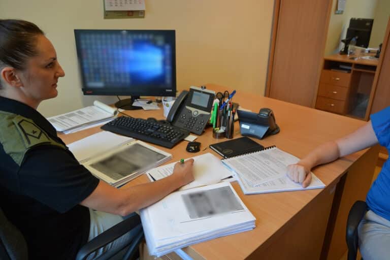 Funkcjonariuszka sprawdza dokumenty cudzoziemca podczas kontroli na biurku.