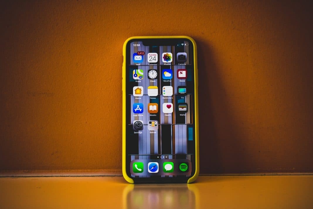 Smartfon z aplikacjami randkowymi na tle pomarańczowej ściany.