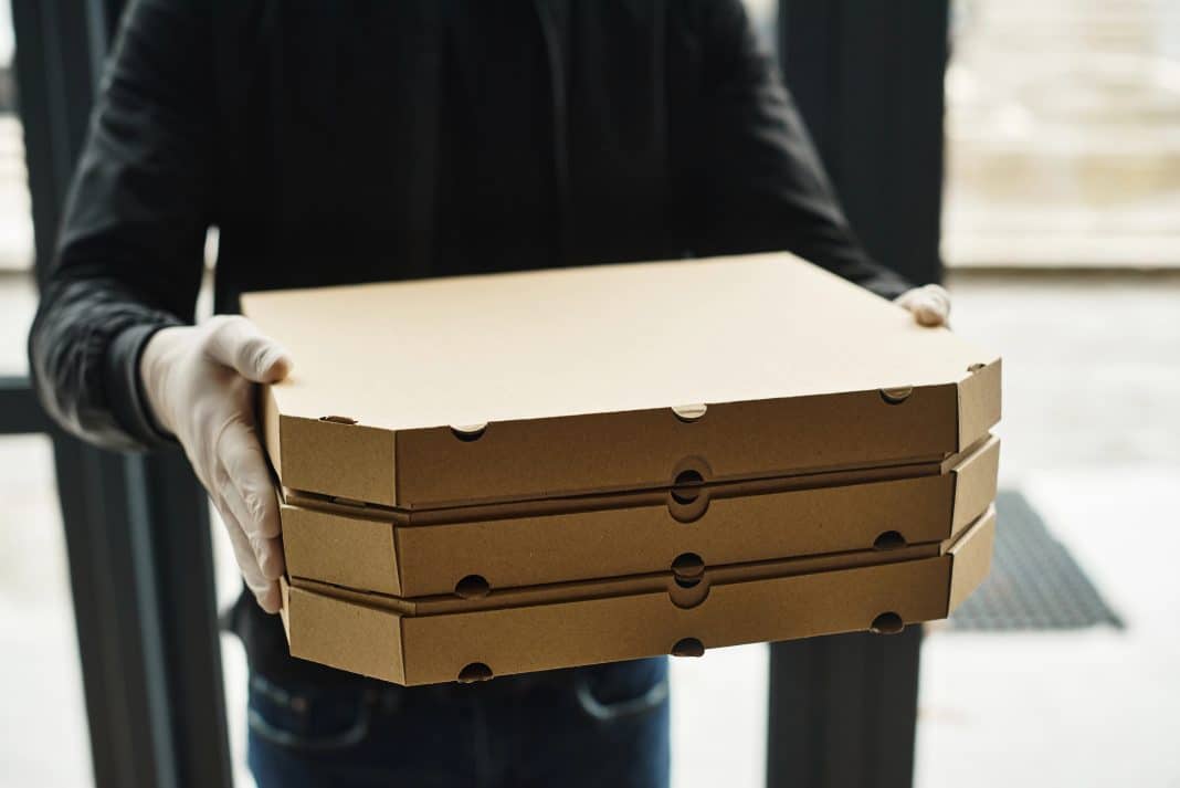 A delivery man wearing gloves carries neatly stacked boxes into an office setting.