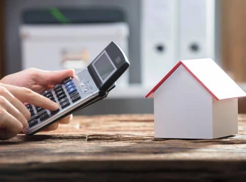 Human Hand Using Calculator With House Model On Wooden Desk