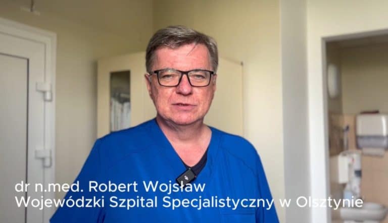Lekarz w niebieskim kitlu i okularach na tle gabinetu w szpitalu.
