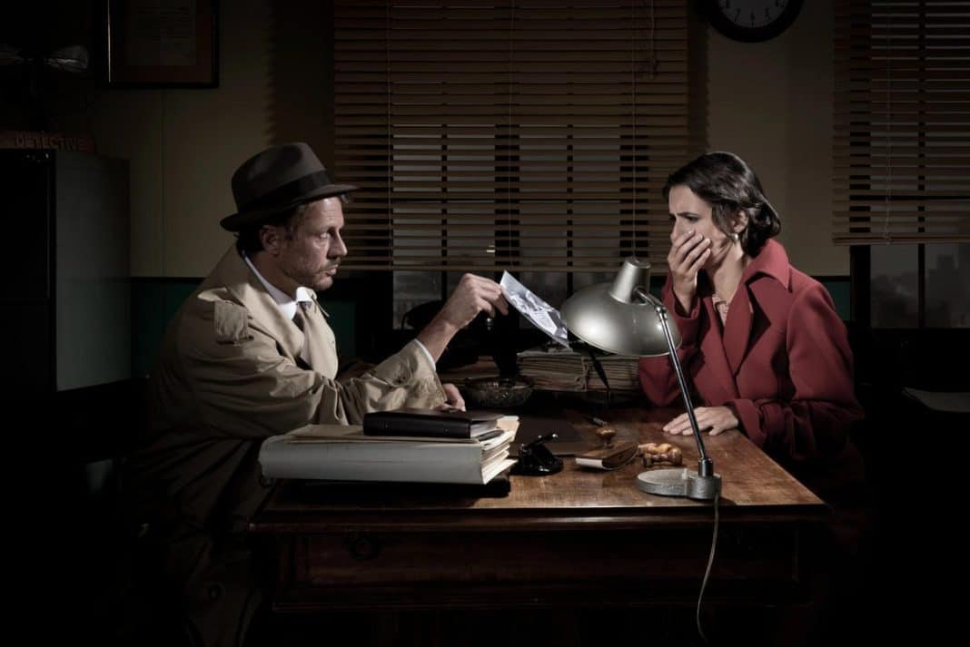 Mężczyzna i kobieta w biurze podczas rozmowy, kobieta zakrywa twarz ręką, mężczyzna trzyma zdjęcie.