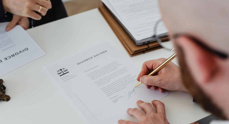 Osoba podpisująca dokument rozwodowy w biurze, obok leży teczka i laptop.