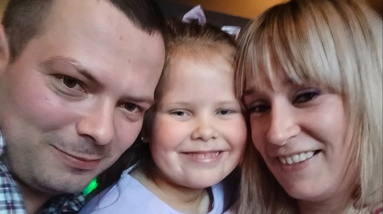 Zdjęcie rodziny: mężczyzna, dziewczynka i kobieta uśmiechają się do kamery.