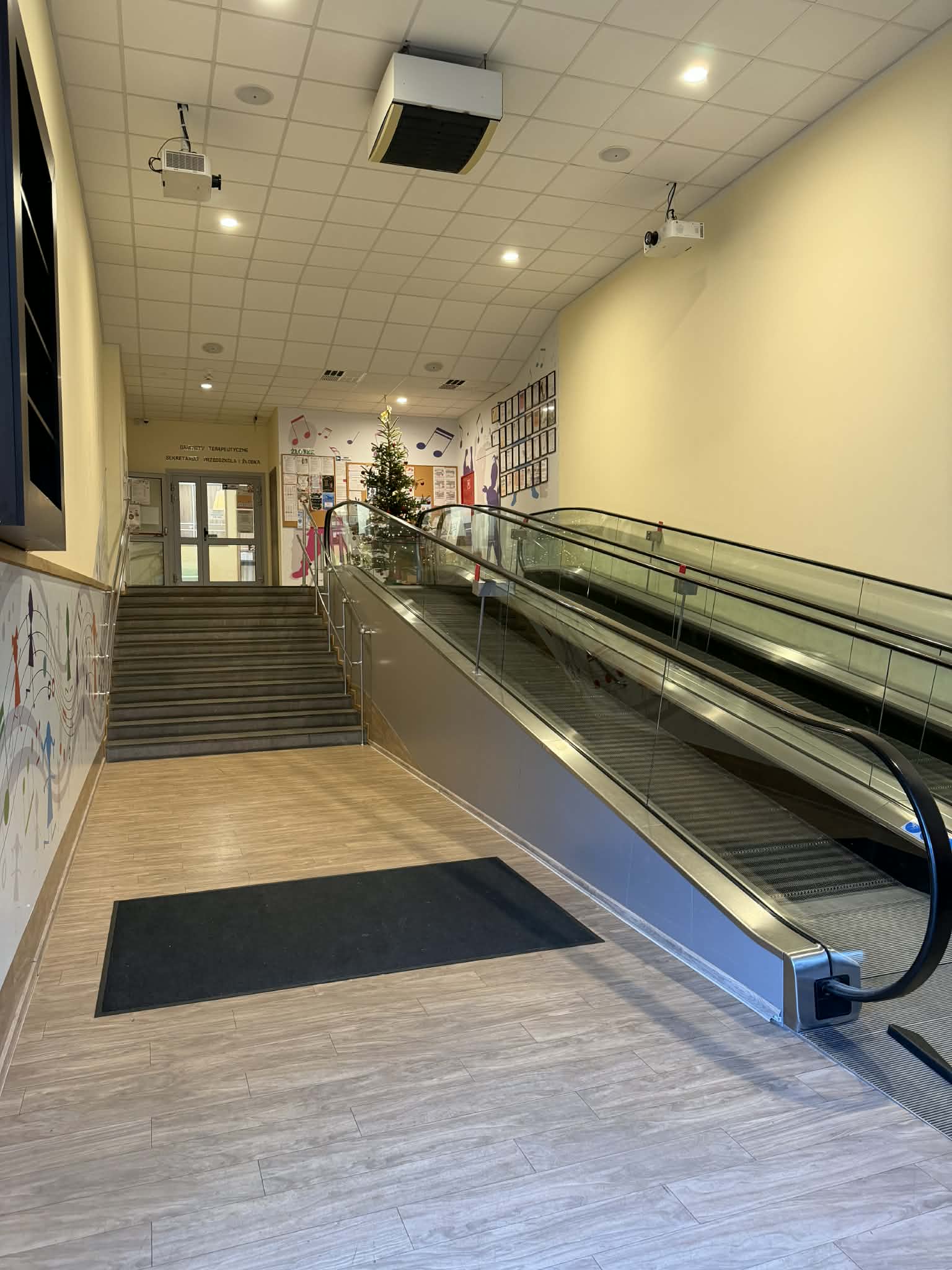 Wnętrze szkoły artystycznej z ruchomymi schodami i dekoracjami na ścianach.