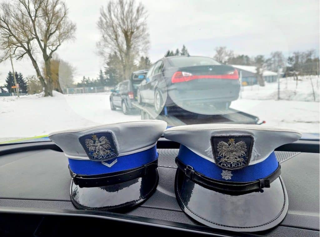 Policja na patrolu na zamarzniętym jeziorze, na pierwszym planie czapki policyjne na desce rozdzielczej.