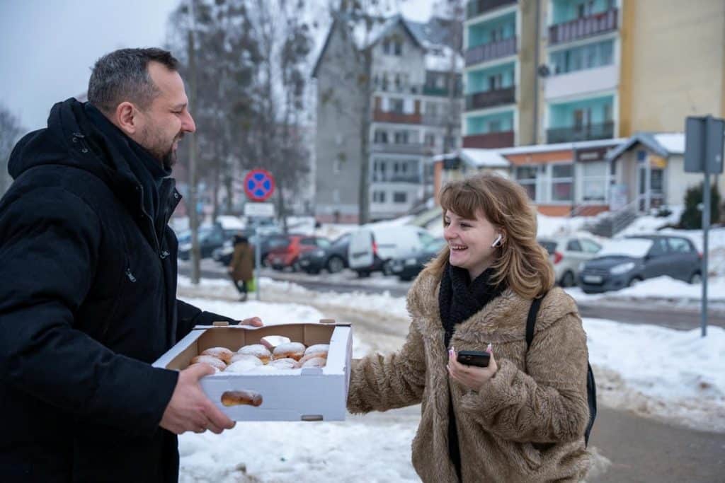 Prezydent Olsztyna rozdaje pączki na ulicy w zimowej scenerii.