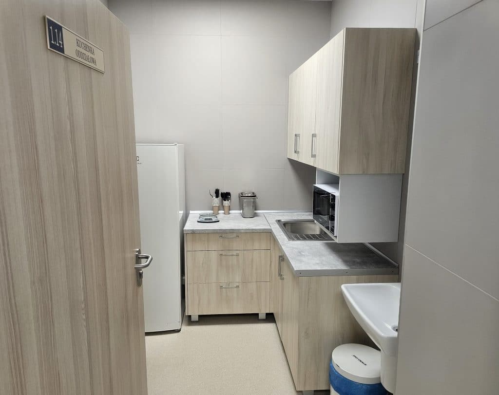 Nowa kuchnia w szpitalu dziecięcym w Olsztynie, wyposażona w szafki, mikrofal&oacute;wkę i zlew.