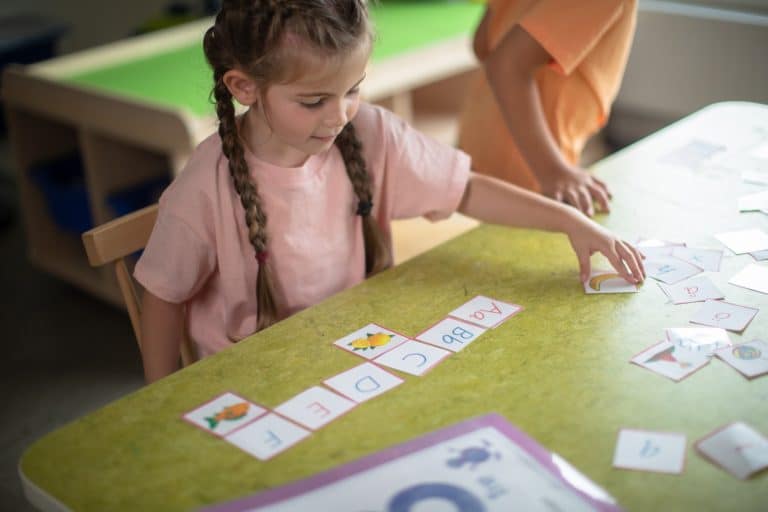 Dziecko bawi się i uczy w przedszkolu, układając karty edukacyjne na zielonym stole.