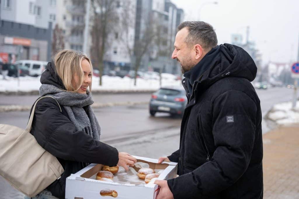 Prezydent Olsztyna rozdaje pączki mieszkańcom na ulicy w centrum miasta.