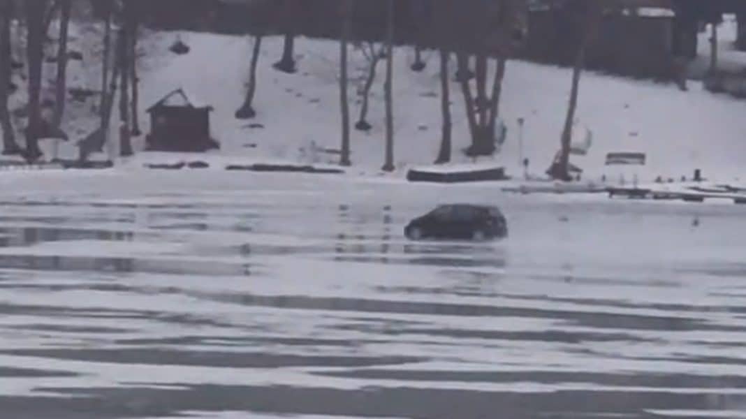 Samoch&oacute;d pędzi po zamarzniętym Jezioraku podczas odwilży, w tle drzewa i śnieg.