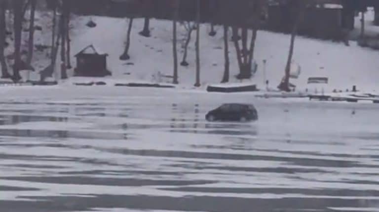 Samoch&oacute;d pędzi po zamarzniętym Jezioraku podczas odwilży, w tle drzewa i śnieg.