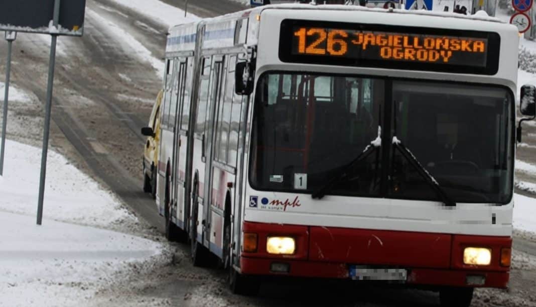 Autobus komunikacji miejskiej na śnieżnej ulicy, w tle znaki drogowe, zimowa pogoda.