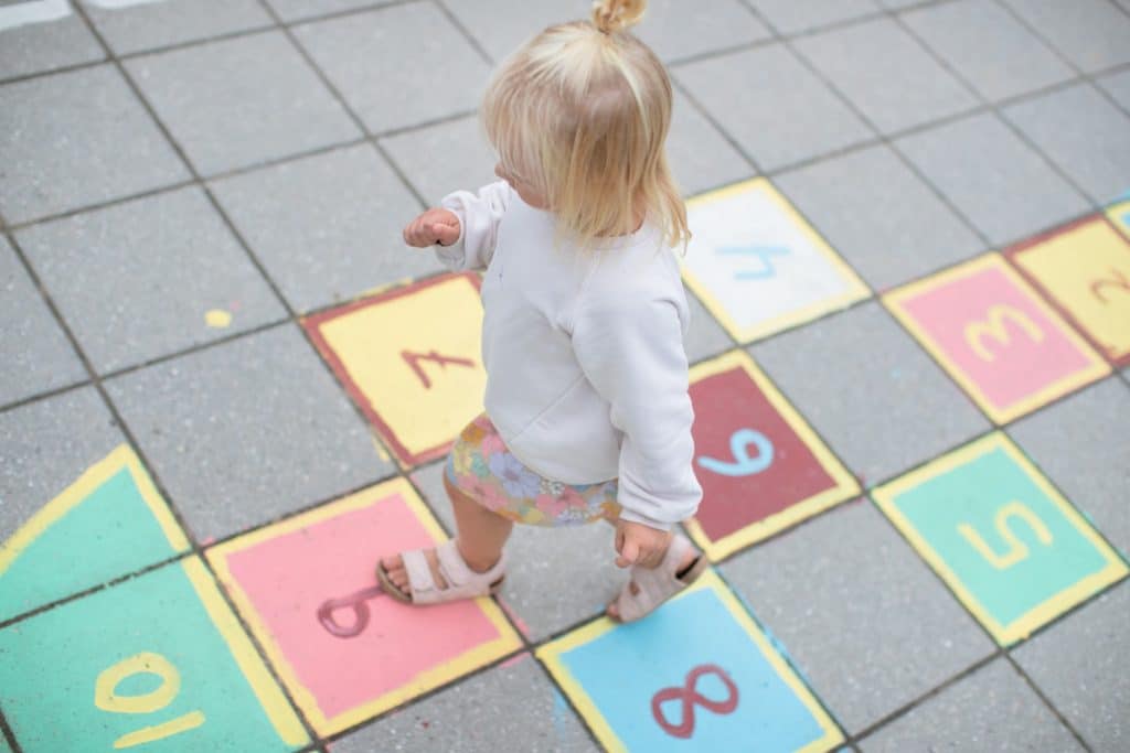 Dziecko bawi się na kolorowym placu zabaw z planszą do gry, widoczne kostki i liczby na podłożu.